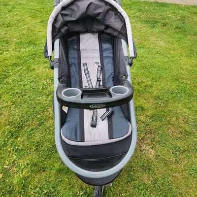 Sale Photo Thumbnail #76: Baby Trend jogging stroller featuring a three-wheel design for enhanced maneuverability. The frame is constructed with durable gray metal, and the seat is black with gray accents. Includes a front tray with cup holders, large under-seat storage basket, an