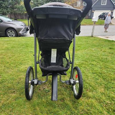 Sale Photo Thumbnail #78: Baby Trend jogging stroller featuring a three-wheel design for enhanced maneuverability. The frame is constructed with durable gray metal, and the seat is black with gray accents. Includes a front tray with cup holders, large under-seat storage basket, an