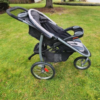 Sale Photo Thumbnail #77: Baby Trend jogging stroller featuring a three-wheel design for enhanced maneuverability. The frame is constructed with durable gray metal, and the seat is black with gray accents. Includes a front tray with cup holders, large under-seat storage basket, an