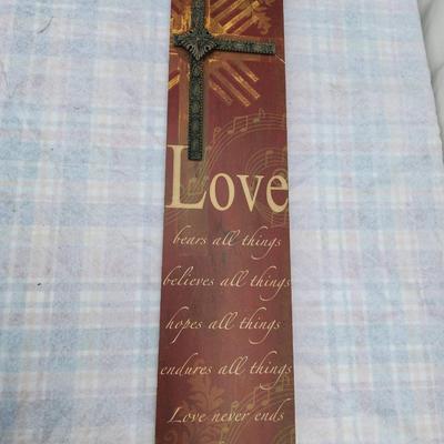 Sale Photo Thumbnail #108: Wooden wall decor featuring a raised cross design with a metallic finish. Includes a printed verse reading "Love bears all things, believes all things, hopes all things, endures all things. Love never ends" from 1 Corinthians 13:7. Measures approximately 
