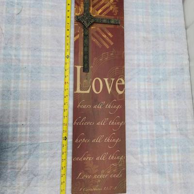 Sale Photo Thumbnail #109: Wooden wall decor featuring a raised cross design with a metallic finish. Includes a printed verse reading "Love bears all things, believes all things, hopes all things, endures all things. Love never ends" from 1 Corinthians 13:7. Measures approximately 