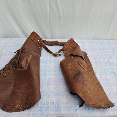 Sale Photo Thumbnail #34: Rugged leather chaps featuring fringe accents and a utility pocket. Adjustable buckle straps ensure a customizable fit. The leather shows visible signs of use and wear, including scuff marks and discoloration, indicating prior practical use. The chaps are