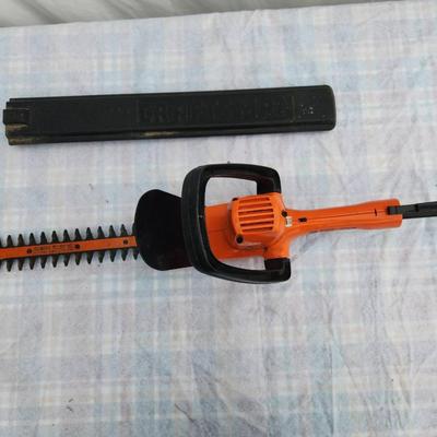 Sale Photo Thumbnail #119: Black & Decker 16-inch electric hedge trimmer featuring an orange body with a black handle. Includes a protective blade cover. Corded design (cord not included). Model number and year of manufacture are not specified. Appears to be in used condition.
