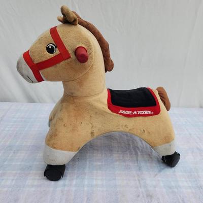 Sale Photo Thumbnail #89: Plush ride-on horse rocker with a tan body, red bridle, black saddle, and black feet. The rocker features sturdy construction and offers handles for grip. Suitable for toddlers, providing a fun and interactive play experience. Approximately toddler-sized;