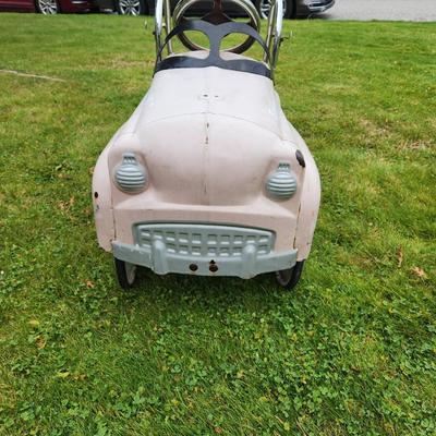 Sale Photo Thumbnail #12: Antique Pink pedal car featuring 'Fire and Rescue' and 'Engine No 7' decals, a metal body, and chrome accents, including handlebars and steering wheel. Designed with a spacious back area and working pedal system. The car shows signs of use, including visi