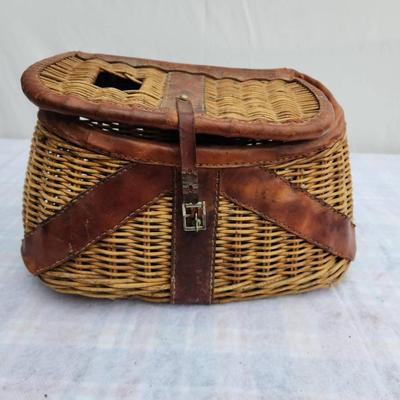 Sale Photo Thumbnail #146: Wicker fishing creel with leather trim and straps, featuring a lid with a slot for fish entry and a buckle closure mechanism for securing the contents. The creel is designed for outdoor fishing use, with carrying straps for convenience. In used condition,