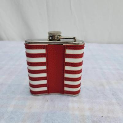 Sale Photo Thumbnail #156: Stainless steel flask featuring an American flag design with stars and stripes wrapped around the exterior. The flask includes a screw-top lid attached by a hinge. Suitable as a collectible or functional item. Details about capacity or manufacturer are no