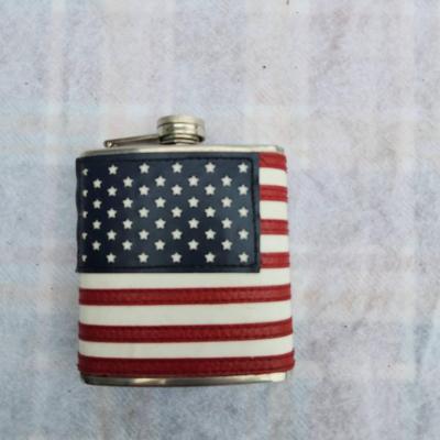 Sale Photo Thumbnail #155: Stainless steel flask featuring an American flag design with stars and stripes wrapped around the exterior. The flask includes a screw-top lid attached by a hinge. Suitable as a collectible or functional item. Details about capacity or manufacturer are no