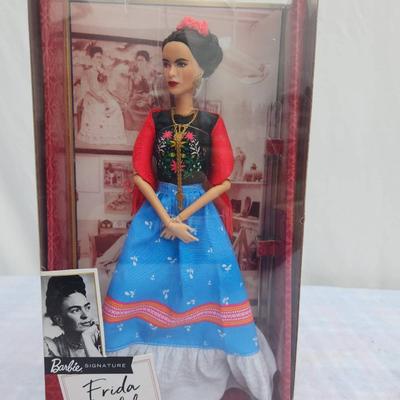 Sale Photo Thumbnail #19: Barbie Inspiring Women Series doll honoring the artist Frida Kahlo (1907-1954). The doll comes dressed in a vibrant outfit inspired by her iconic style, featuring a red blouse, blue skirt, and accessories. It is housed in its original packaging, which inc