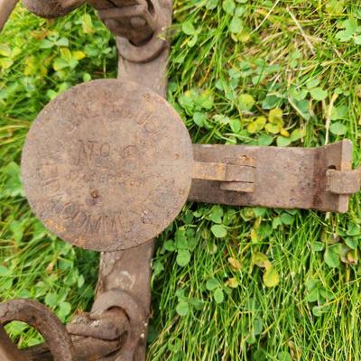 Sale Photo Thumbnail #29: Three vintage iron animal traps featuring attached chains. Each trap is constructed from heavy iron and displays wear from age and use, including rust and patina. The design includes trigger mechanisms and stamped markings on the pressure plates, with fai