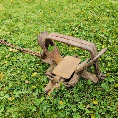 Sale Photo Thumbnail #32: Two vintage metal animal traps with attached chains. The set includes one cylindrical and one rectangular trap, each exhibiting rust and wear consistent with age and use. Both traps are intact with all moving parts. Each trap is connected to a chain that 