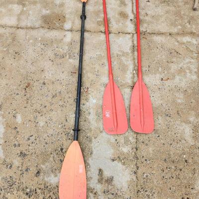 Sale Photo Thumbnail #183: Three oars, including a dual-blade black and red kayak paddle with a center connecting rod, and two single-blade red paddle boat oars with T-shaped handles. Made of plastic or composite material. Visible signs of wear consistent with regular use, such as 