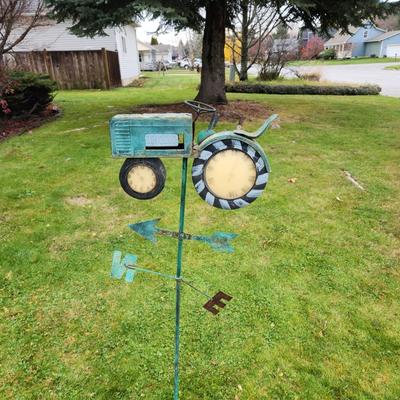 Sale Photo Thumbnail #186: Decorative metal weathervane featuring a tractor motif with clock faces integrated into the front and rear wheels. The piece is weathered for a rustic look and includes directional markers for North, East, South, and West. Designed for outdoor installatio
