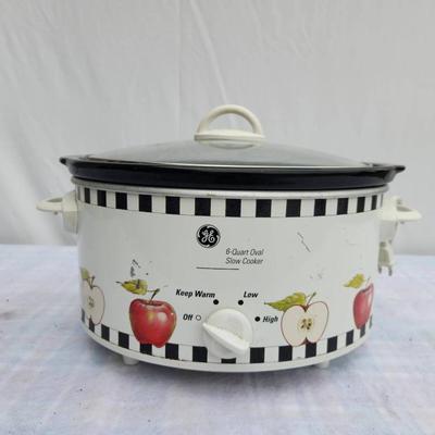 Sale Photo Thumbnail #207: General Electric (GE) slow cooker featuring an apple design with black-and-white checkered trim. Includes a removable ceramic inner pot, glass lid with handle, and a dial for settings (off, warm, low, and high). Appears intact with visible use. Suitable f