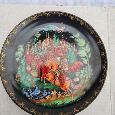 Sale Photo Thumbnail #213: Russian hand-painted lacquerware plate featuring a vibrant fairy tale scene with a horse and castle motif. The reverse side includes inscriptions in Cyrillic detailing the plate's origins and theme. Accompanied by documentation, illustrations, and origina