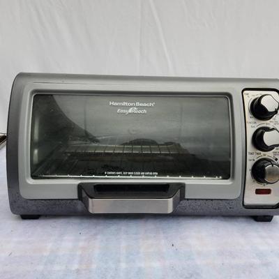 Sale Photo Thumbnail #217: Hamilton Beach Easy Reach toaster oven featuring a roll-top door for convenient access. Includes adjustable temperature control knobs, a wire rack, crumb tray, and additional wire baskets. Shows signs of use with visible surface discoloration and residue.