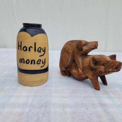 Sale Photo Thumbnail #220: A small ceramic jar labeled 'Harley money,' featuring a yellow body with a blue heart and band accent, alongside a wooden figurine of two pigs in a playful pose. The jar serves as a coin holder or decoration, while the wooden carving showcases detailed cr