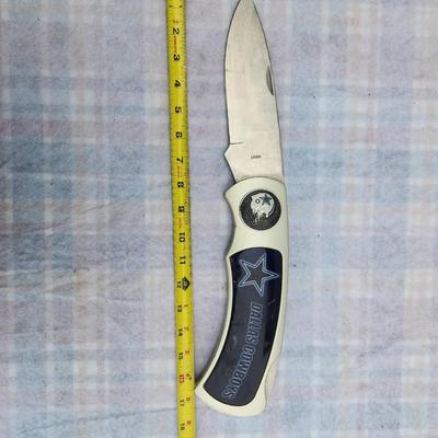 Sale Photo Thumbnail #227: Dallas Cowboys folding knife featuring a white handle with a decorative star emblem and the team's name in blue. The blade is stainless steel, and the knife measures approximately 8 inches when open and about 4.5 inches when folded. The item includes a de