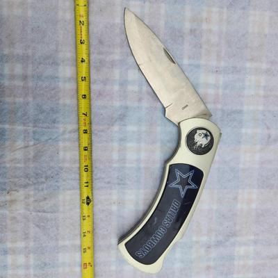 Sale Photo Thumbnail #228: Dallas Cowboys folding knife featuring a white handle with a decorative star emblem and the team's name in blue. The blade is stainless steel, and the knife measures approximately 8 inches when open and about 4.5 inches when folded. The item includes a de