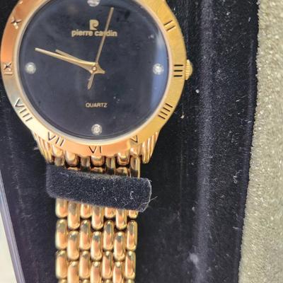 Sale Photo Thumbnail #234: Pierre Cardin gold-tone quartz watch featuring a black dial with a Roman numeral bezel and four crystals at the 3, 6, 9, and 12 o'clock positions. It comes with a multi-link gold-tone bracelet. Presented in its original box with tag attached. No visible d