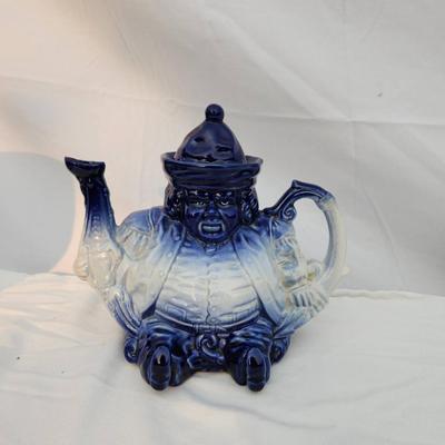 Sale Photo Thumbnail #239: Blue and white ceramic figural teapot, featuring a seated figure design. The teapot includes a removable lid and is hand-painted with gradient blue tones transitioning to white. Measuring tools shown suggest approximate size; exact dimensions are unstated