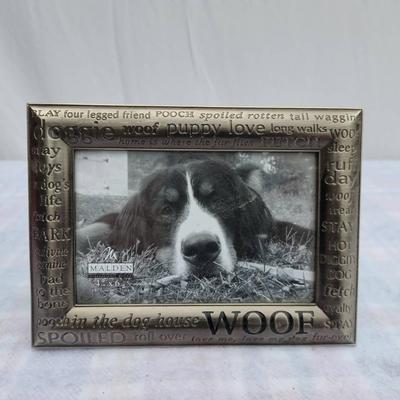 Sale Photo Thumbnail #241: Silver-tone decorative frame with embossed dog-centric phrases, including 'WOOF' and 'Spoiled Rotten'. Features a textured design and an integrated stand for tabletop display. Includes a photo insert of a dog. Material and manufacturer are not specified. 