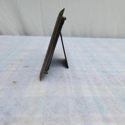 Sale Photo Thumbnail #242: Silver-tone decorative frame with embossed dog-centric phrases, including 'WOOF' and 'Spoiled Rotten'. Features a textured design and an integrated stand for tabletop display. Includes a photo insert of a dog. Material and manufacturer are not specified. 