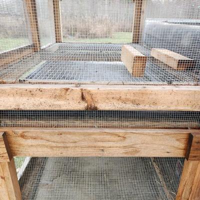 Sale Photo Thumbnail #46: A wooden quail cage with two levels, featuring wire mesh sides and bottoms for ventilation and waste management. The cage includes hinged front doors for easy access and a slanted green metal roof for weather protection. Supported by four wooden legs, it 