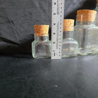 Two large serving bowls a glass cake pan, strainer and 5 square glass containers with cork stoppers