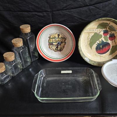 Two large serving bowls a glass cake pan, strainer and 5 square glass containers with cork stoppers