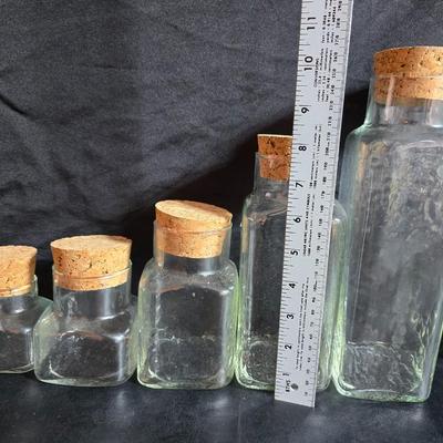 Two large serving bowls a glass cake pan, strainer and 5 square glass containers with cork stoppers