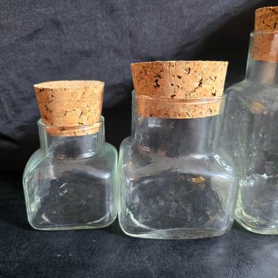 Two large serving bowls a glass cake pan, strainer and 5 square glass containers with cork stoppers