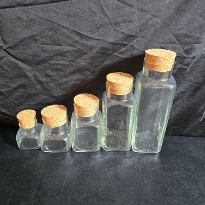 Two large serving bowls a glass cake pan, strainer and 5 square glass containers with cork stoppers