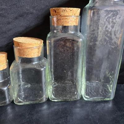 Two large serving bowls a glass cake pan, strainer and 5 square glass containers with cork stoppers