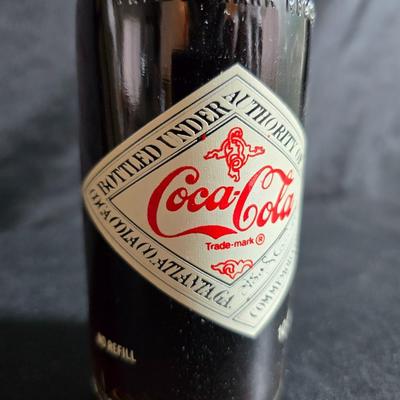 Working 1970s Coca-Cola wall clock with a faux wood grain plastic frame and a commemorative Coca-Cola bottle from the 1984 Summer...