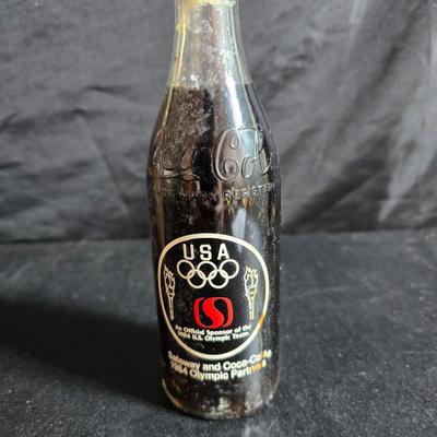 Working 1970s Coca-Cola wall clock with a faux wood grain plastic frame and a commemorative Coca-Cola bottle from the 1984 Summer...