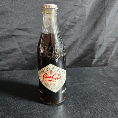Working 1970s Coca-Cola wall clock with a faux wood grain plastic frame and a commemorative Coca-Cola bottle from the 1984 Summer...