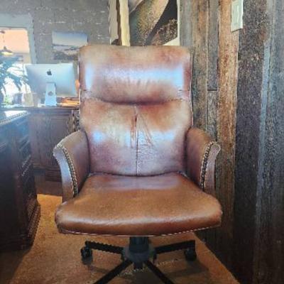 Sale Photo Thumbnail #12: Leather office chair featuring a padded seat, backrest, and armrests. The chair is upholstered in a distressed leather finish with nailhead trim detail. It includes a rolling base with five casters and an adjustable height mechanism for comfort and functi