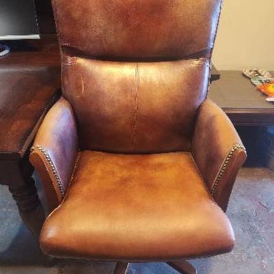 Sale Photo Thumbnail #9: Leather office chair featuring a padded seat, backrest, and armrests. The chair is upholstered in a distressed leather finish with nailhead trim detail. It includes a rolling base with five casters and an adjustable height mechanism for comfort and functi