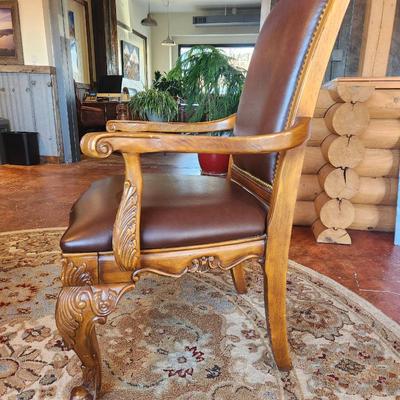 Sale Photo Thumbnail #23: Wooden dining table set measuring 6x3x2.6 feet, featuring a glass top and ornate carved detailing on the legs. Includes six chairs with padded seats and backs, upholstered in brown leather-like material, and armrests. Each chair displays detailed carvings