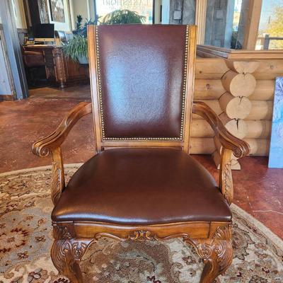 Sale Photo Thumbnail #22: Wooden dining table set measuring 6x3x2.6 feet, featuring a glass top and ornate carved detailing on the legs. Includes six chairs with padded seats and backs, upholstered in brown leather-like material, and armrests. Each chair displays detailed carvings