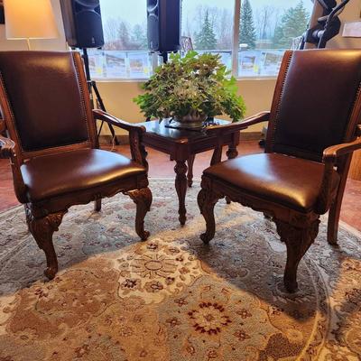 Sale Photo Thumbnail #21: Wooden dining table set measuring 6x3x2.6 feet, featuring a glass top and ornate carved detailing on the legs. Includes six chairs with padded seats and backs, upholstered in brown leather-like material, and armrests. Each chair displays detailed carvings