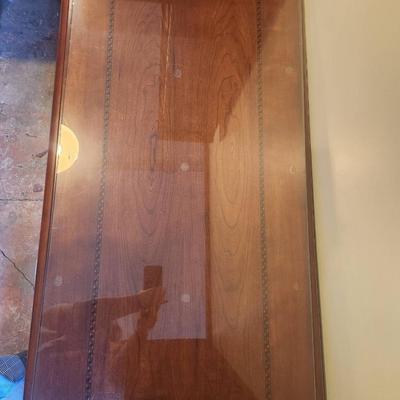 Sale Photo Thumbnail #25: Rectangular wooden coffee table featuring a protective glass top overlay. The table displays decorative inlay detailing on its surface and rests on four sturdy turned legs. Condition appears to be good with minimal signs of wear. Suitable for both functio