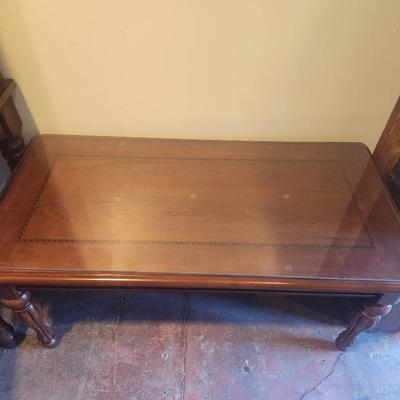 Sale Photo Thumbnail #26: Rectangular wooden coffee table featuring a protective glass top overlay. The table displays decorative inlay detailing on its surface and rests on four sturdy turned legs. Condition appears to be good with minimal signs of wear. Suitable for both functio