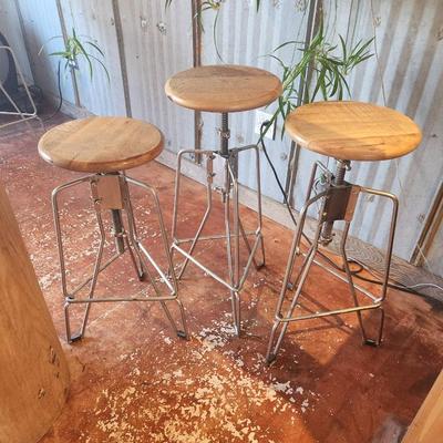 Sale Photo Thumbnail #38: Three bar stools featuring round seats crafted from mango wood. The stools are mounted on sturdy metal bases with an adjustable screw mechanism for height changes. The base design incorporates a minimalist aesthetic, with footrests for added comfort. Thes