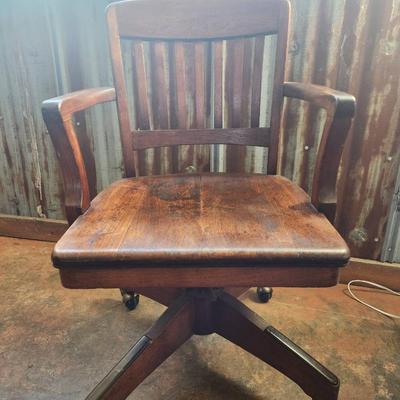 Sale Photo Thumbnail #41: Solid wood office chair featuring a slat back design, fixed armrests, and a four-leg base with casters for mobility. The finish exhibits signs of wear, including discoloration and surface scratches, consistent with use. Classic functional style suitable f