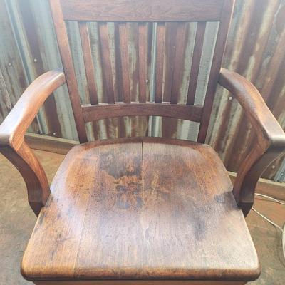 Sale Photo Thumbnail #42: Solid wood office chair featuring a slat back design, fixed armrests, and a four-leg base with casters for mobility. The finish exhibits signs of wear, including discoloration and surface scratches, consistent with use. Classic functional style suitable f