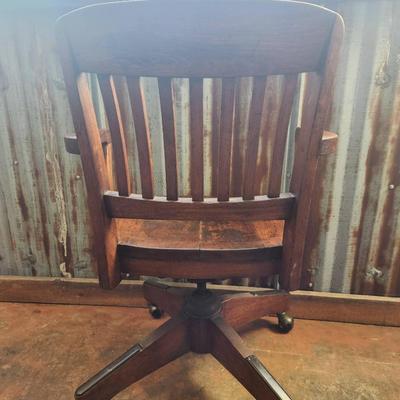 Sale Photo Thumbnail #43: Solid wood office chair featuring a slat back design, fixed armrests, and a four-leg base with casters for mobility. The finish exhibits signs of wear, including discoloration and surface scratches, consistent with use. Classic functional style suitable f