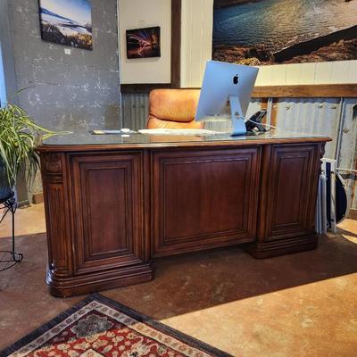Sale Photo Thumbnail #46: Hooker desk crafted from cherry wood, measuring 6 feet in length, 3 feet in width, and 2.6 feet in height. Features include a glass top for added protection, multiple drawers for storage, and elegant carved details. Labeled with Hooker Furniture branding,