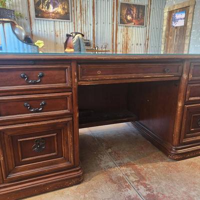 Sale Photo Thumbnail #80: Hooker desk crafted from cherry wood, measuring 6 feet in length, 3 feet in width, and 2.6 feet in height. Features include a glass top for added protection, multiple drawers for storage, and elegant carved details. Labeled with Hooker Furniture branding,